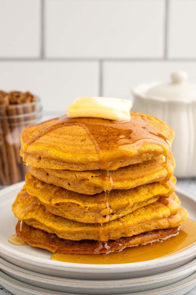 A stack of sweet potato pancakes with a pat of butter and covered in syrup on a white plate on a white background