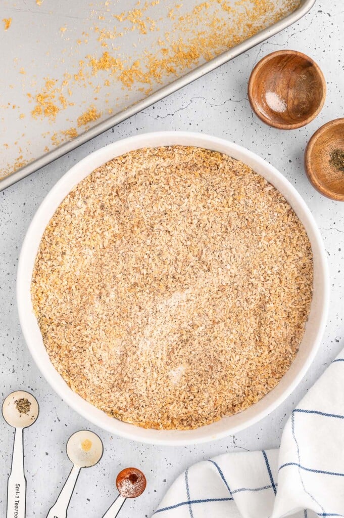 An overhead shot of panko breadcrumbs, flour, and spices in a large white bowl on a white counter with a baking dish on the side