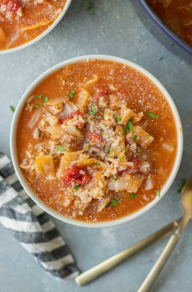 A bowl of stuffed cabbage soup with another bowl of soup and spoons on the side on a grey counter