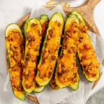 Stuffed Zucchini Boats on a pieces of parchment paper on a wooden cutting board with shredded cheese on the side