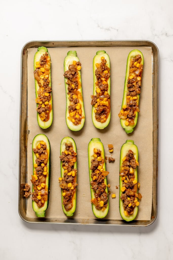 8 uncooked Stuffed Zucchini Boats before the cheese is added on a parchment lined baking dish.