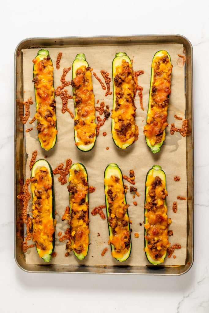 8 Stuffed Zucchini Boats on a parchment lined baking dish just out of the oven with melted cheese.
