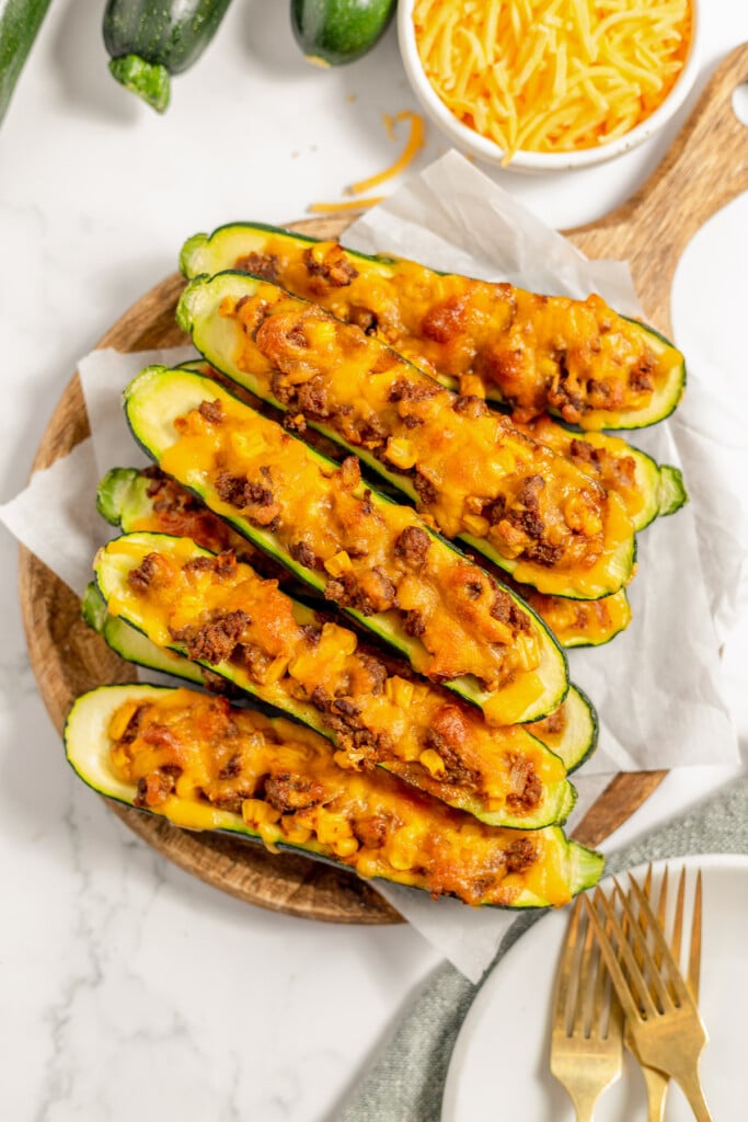 Stuffed Zucchini Boats on a pieces of parchment paper on a wooden cutting board with shredded cheese on the side