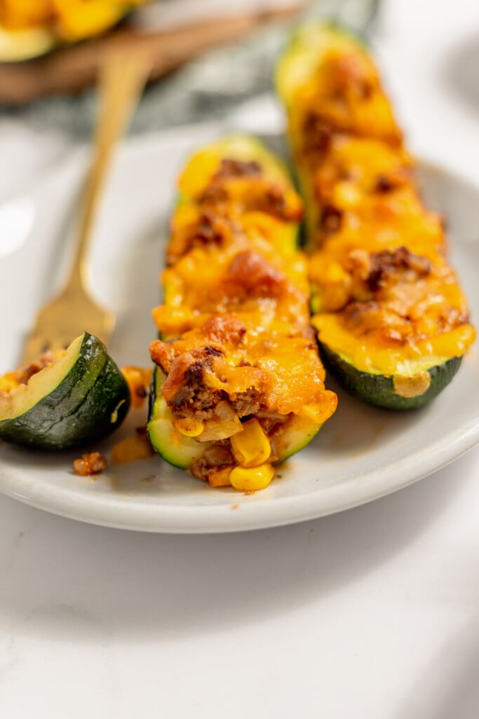 A photo of the side of a taco stuffed zucchini boat that shows the ground beef and corn filling topped with melted cheese on a white plate