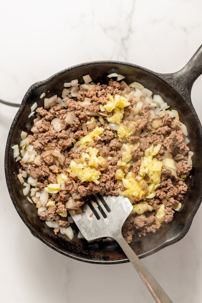 Browned ground beef with onion, and zucchini seedy centers being mixed in with a spatula to make ground beef stuffing for zucchini boats.