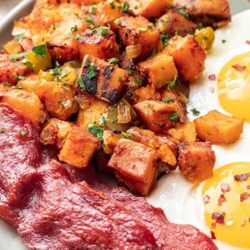 Sweet Potato Home Fries on a grey plate with bacon and sunny side up eggs