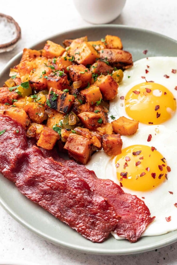 Sweet Potato Home Fries on a grey plate with bacon and sunny side up eggs