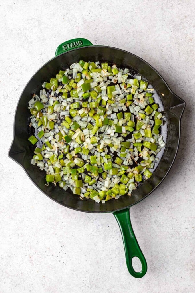 An overhead shot of a cast iron skillet with onion and green bell peppers being sauteed for sweet potato home fries