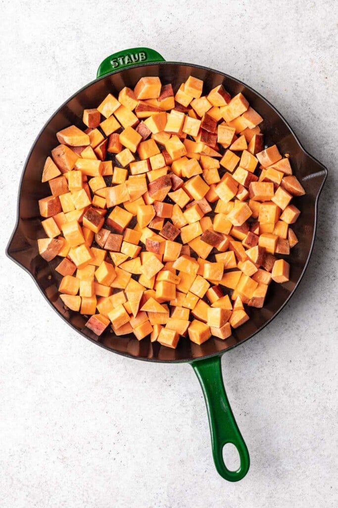 An overhead shot of cubed sweet potatoes in a cast iron skillet for sweet potato home fries