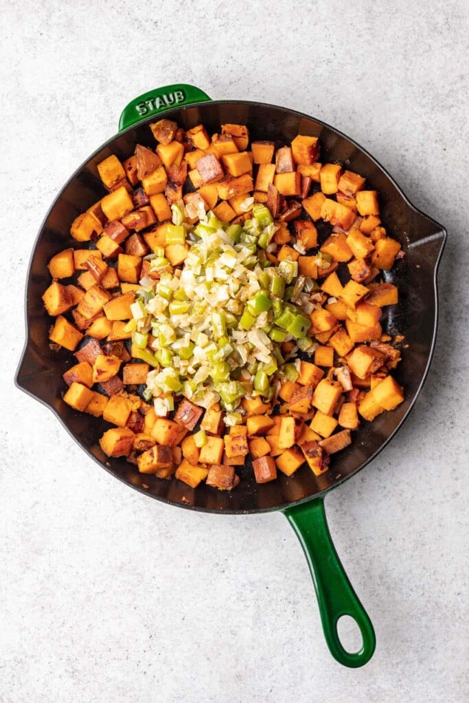 An overhead shot of sauteed onions and bell peppers on top of cooked cubed sweet potatoes to make sweet potato home fries
