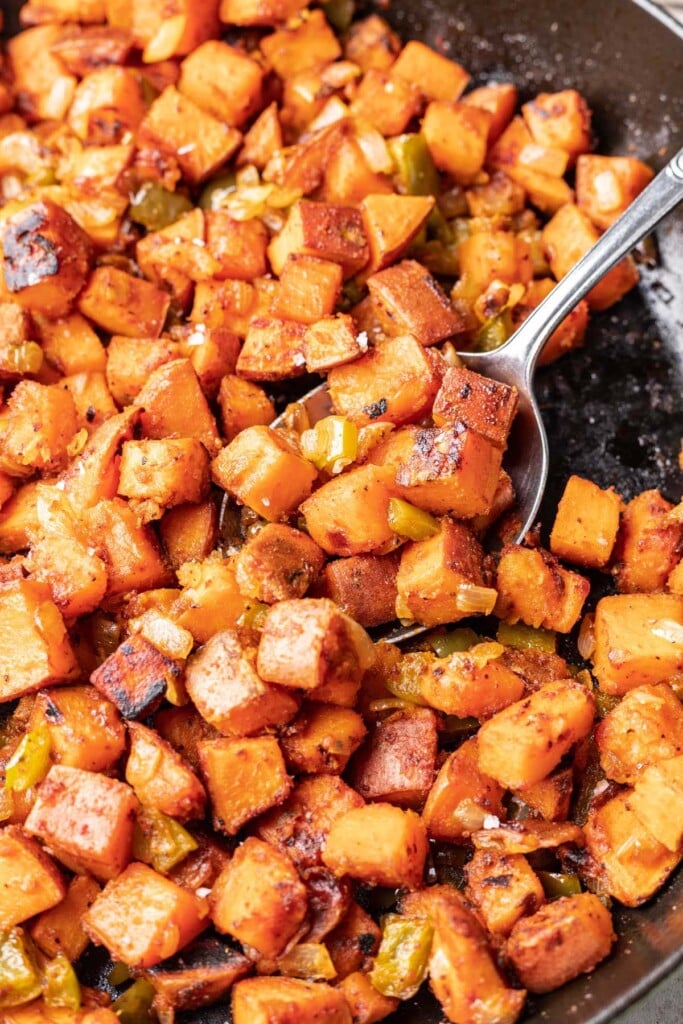 A close up of sweet potato home fries skillet with a spoon taking a scoop out of it