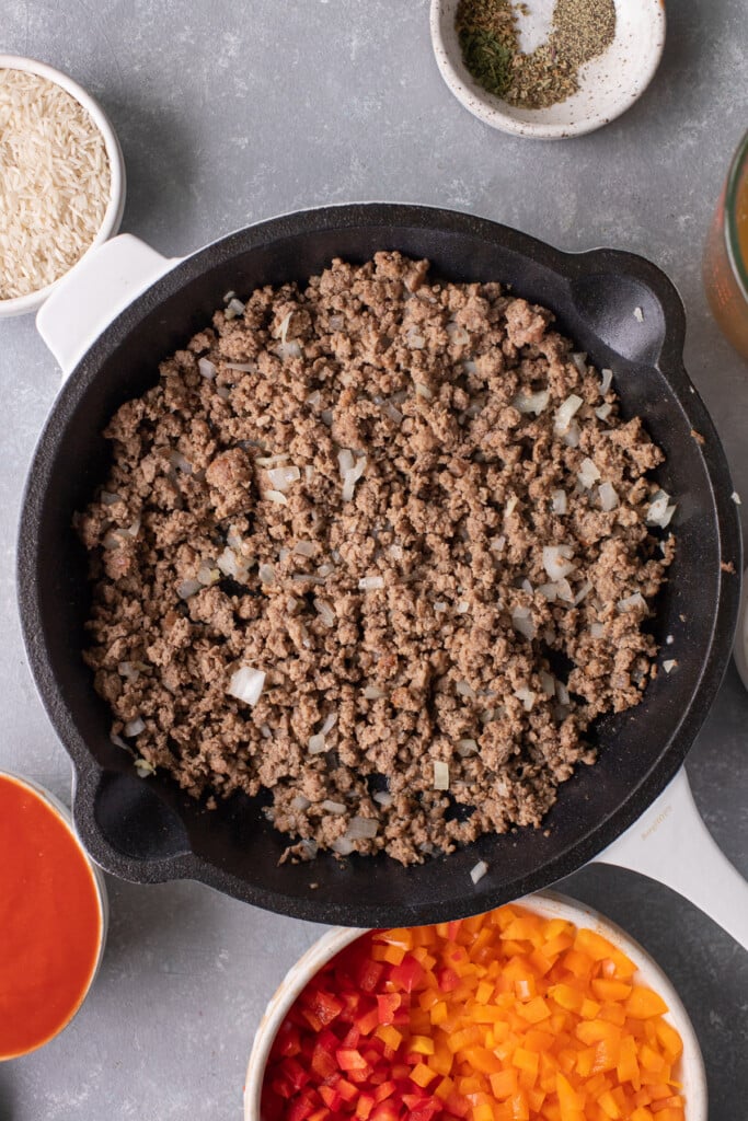 Ground beef, onions, and garlic cooked in a skillet with more ingredients for unstuffed skillet on the side