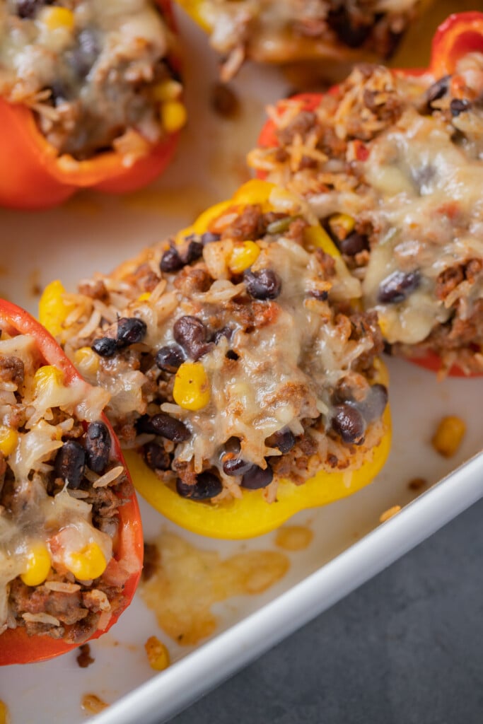 Taco stuffed peppers in a white baking dish on a grey background for a ground beef & rice recipe round up