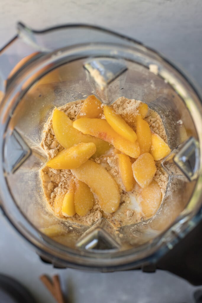 An overhead shot of ingredients for peach smoothie in a vitamix blender before being blended