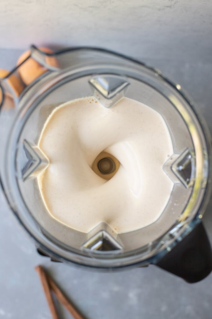 An overhead shot of ingredients for peach smoothie in a vitamix blender while being blended