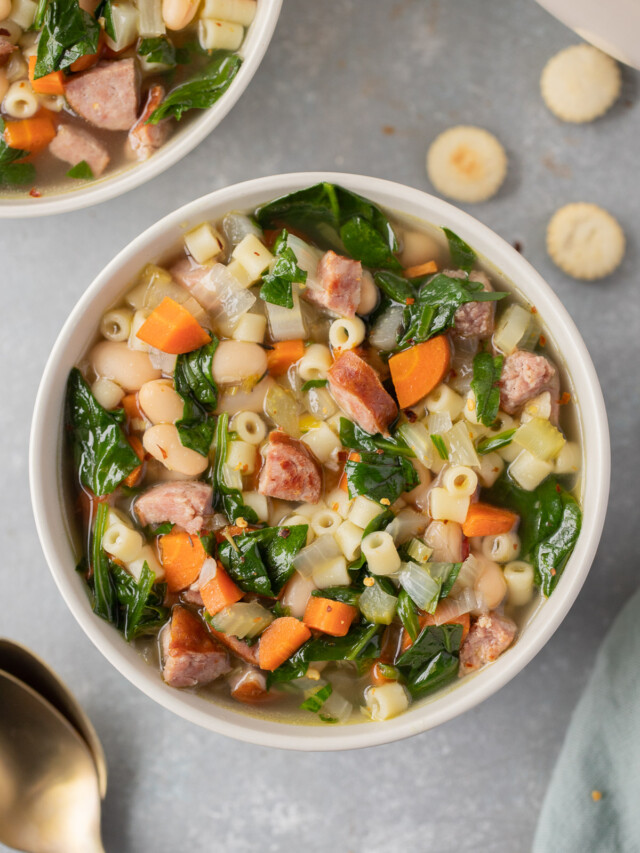 An overhead shot of a bowl of kielbasa soup with another bowl of soup and spoons on the side