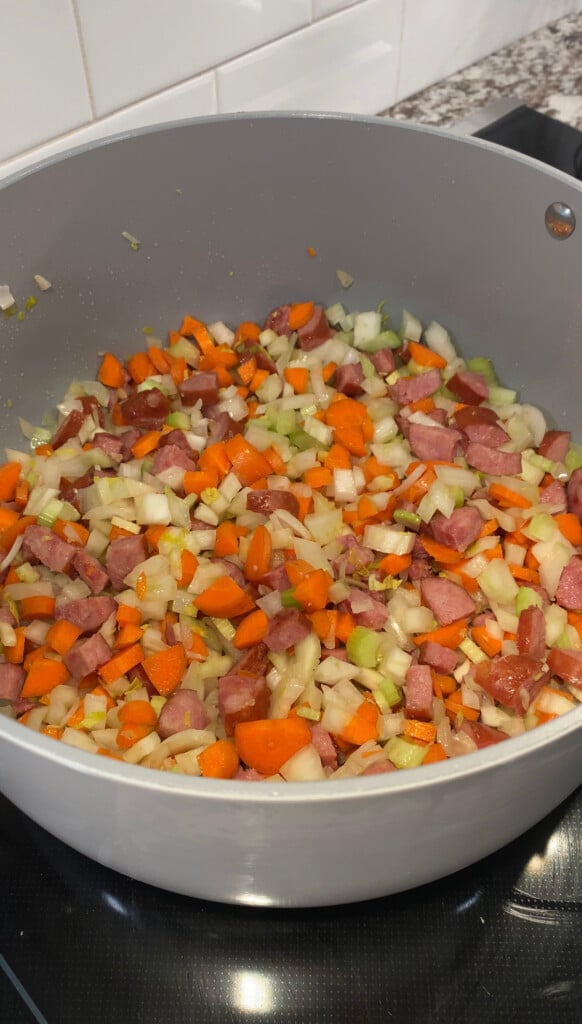 Veggies and kielbasa cooking in a large pot for polish sausage soup in a large pot on a black stove