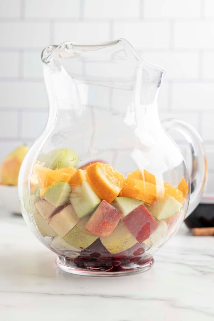 Chopped fruit (green and red apples, oranges, pear) in a clear pitcher before adding wine to make red sangria