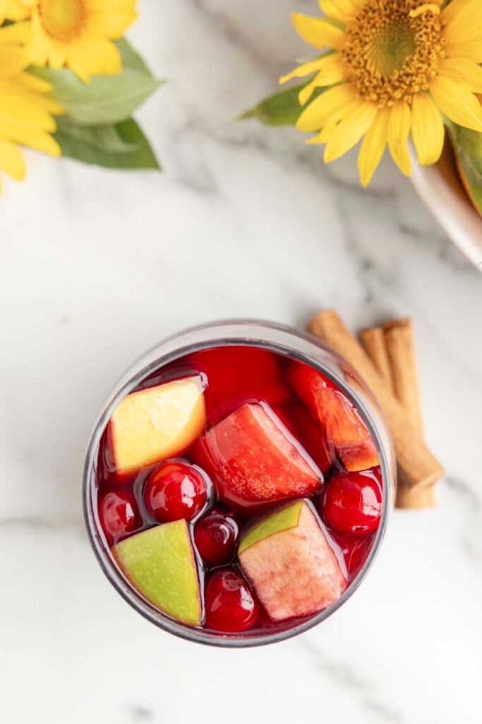Red Wine Sangria in a clear glass with cinnamon sticks and flowers on the side on a marble counter