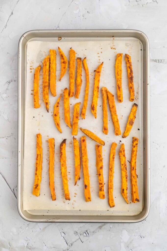 An overhead shot of crispy oven baked sweet potato fries on a parchment lined baking sheet on a marble background