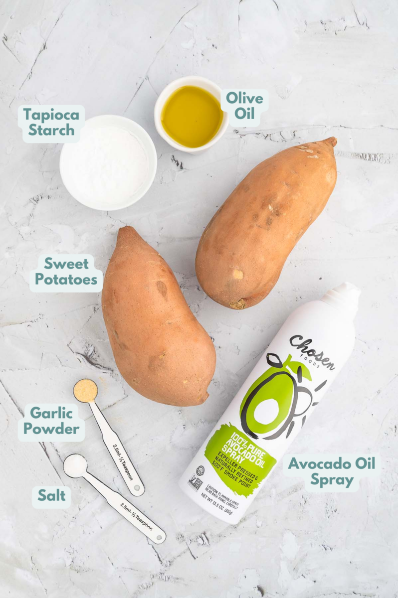 Ingredients for oven baked sweet potato fries on a white background: sweet potatoes, tapioca starch, olive oil, salt, garlic powder, avocado oil spray