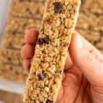 A hand holding up a single healthy homemade granola bar with more bars in the background