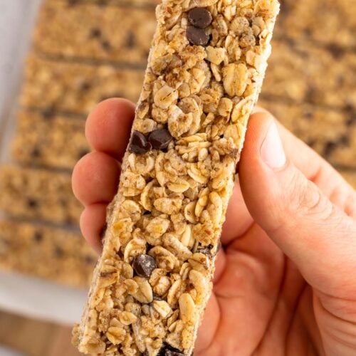A hand holding up a single healthy homemade granola bar with more bars in the background