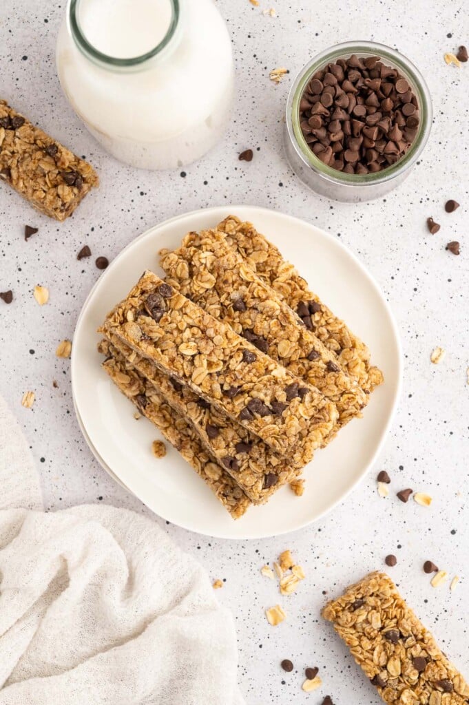 Healthy granola bars stacked on a white plate with a small bowl of chocolate chips on the side
