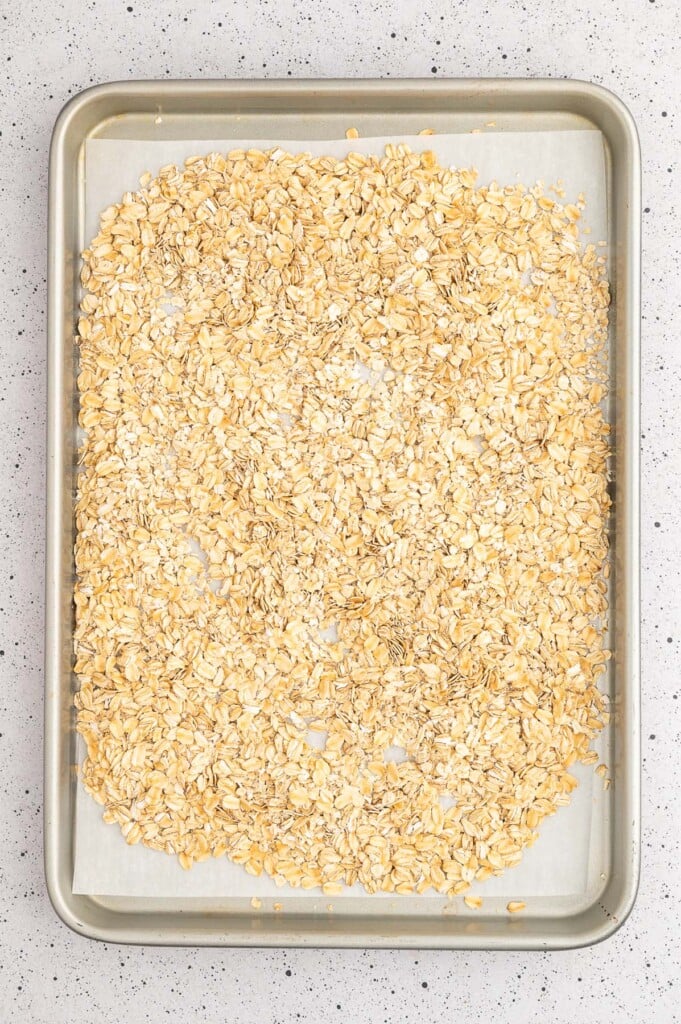 Old-fashioned oats and quick oats on a parchment lined baking sheet getting ready to be toasted to make healthy granola bars