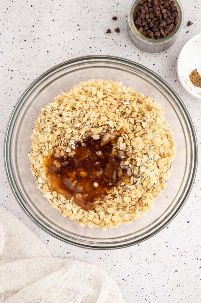 Toasted oats, puffed rice cereal and salt in a clear bowl with a honey/coconut oil mixture poured on top before mixing to make healthy granola bars