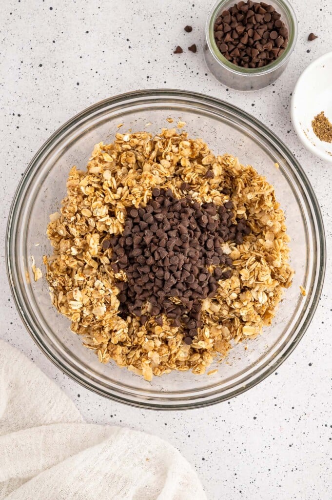 mini chocolate chips on top of healthy granola bar mixture in a clear bowl.