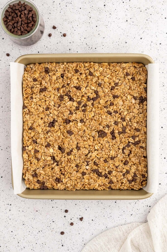 Healthy granola bar mixture pressed into a parchment lined 8x8 baking pan before being cut into bars