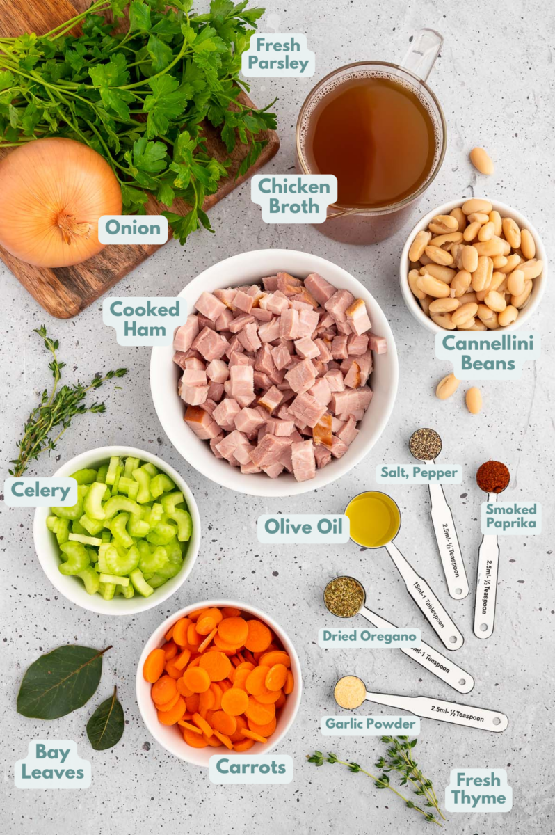 Ingredients for Ham White Bean Soup in small bowls: olive oil, onion, carrots, celery fresh and dried spices, cooked ham, chicken broth, cannellini beans