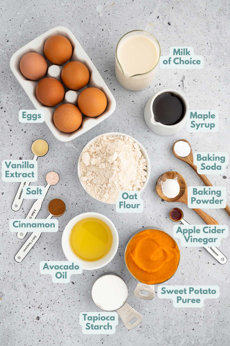 Ingredients for sweet potato pancakes in white bowls: oat flour, tapioca starch, baking soda, baking powder, ground cinnamon, sea salt, sweet potato puree, non-dairy milk, eggs, avocado oil, pure maple syrup, vanilla, apple cider vinegar