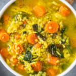 Chicken pastina soup in a white bowl on a grey counter with crackers on the side