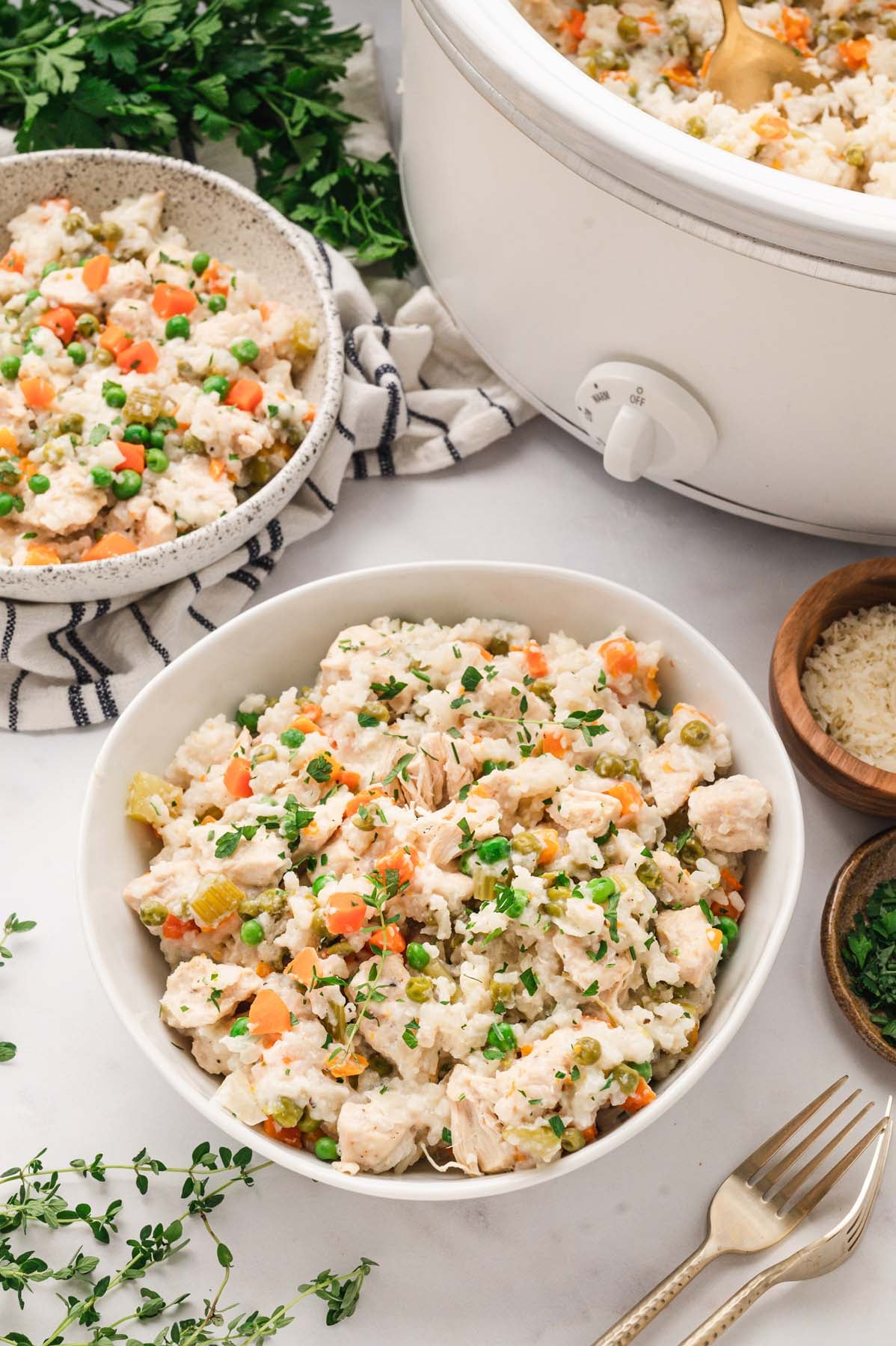 Chicken and rice in crockpot next to two serving bowls of the casserole.