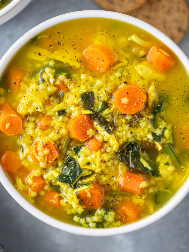Chicken pastina soup in a white bowl on a grey counter with crackers on the side