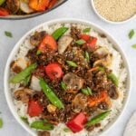 Ground Beef Stir Fry on a bed of rice on a plate with a dutch oven of the stirfry on the side