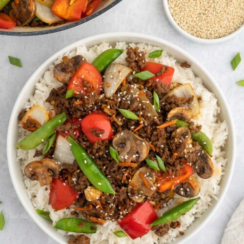 Ground Beef Stir Fry on a bed of rice on a plate with a dutch oven of the stirfry on the side
