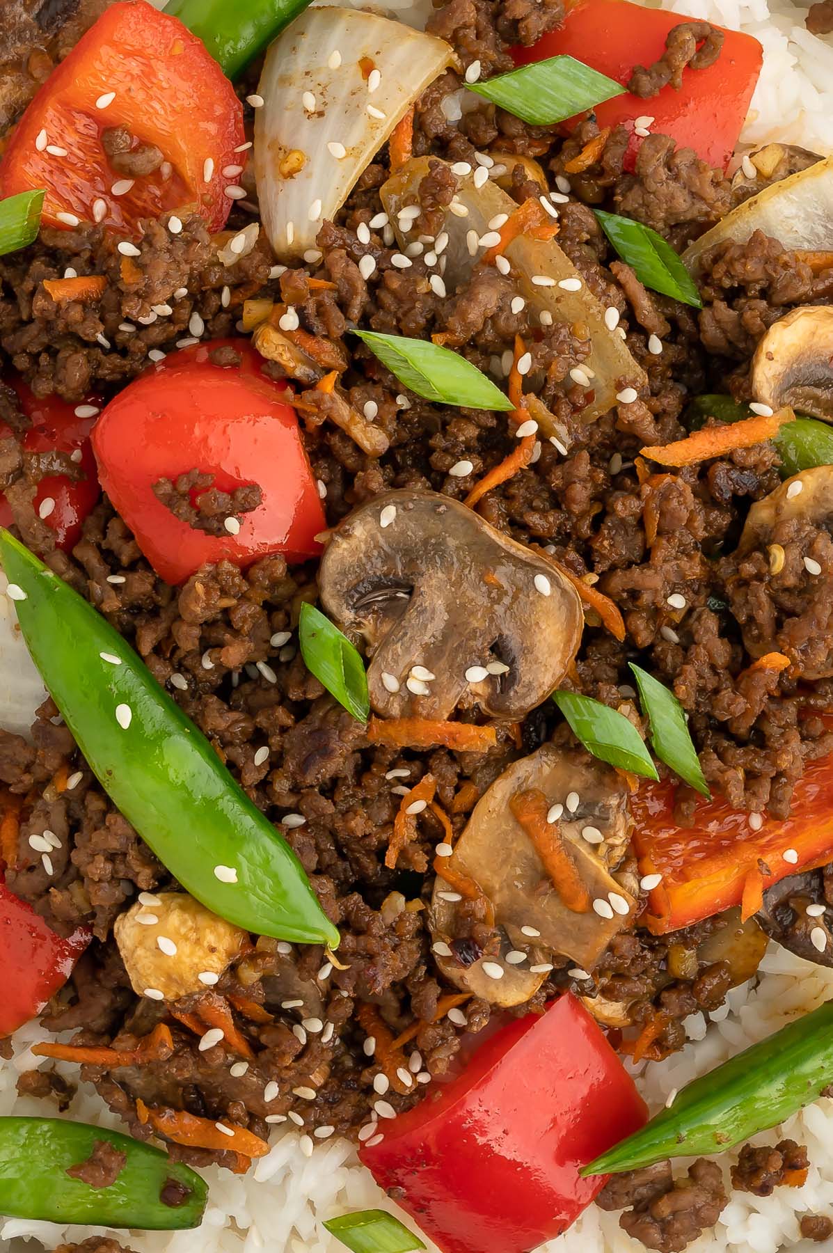 A close up of ground beef stir fry with sugar snap peas, red bell peppers, carrots, and mushrooms. 