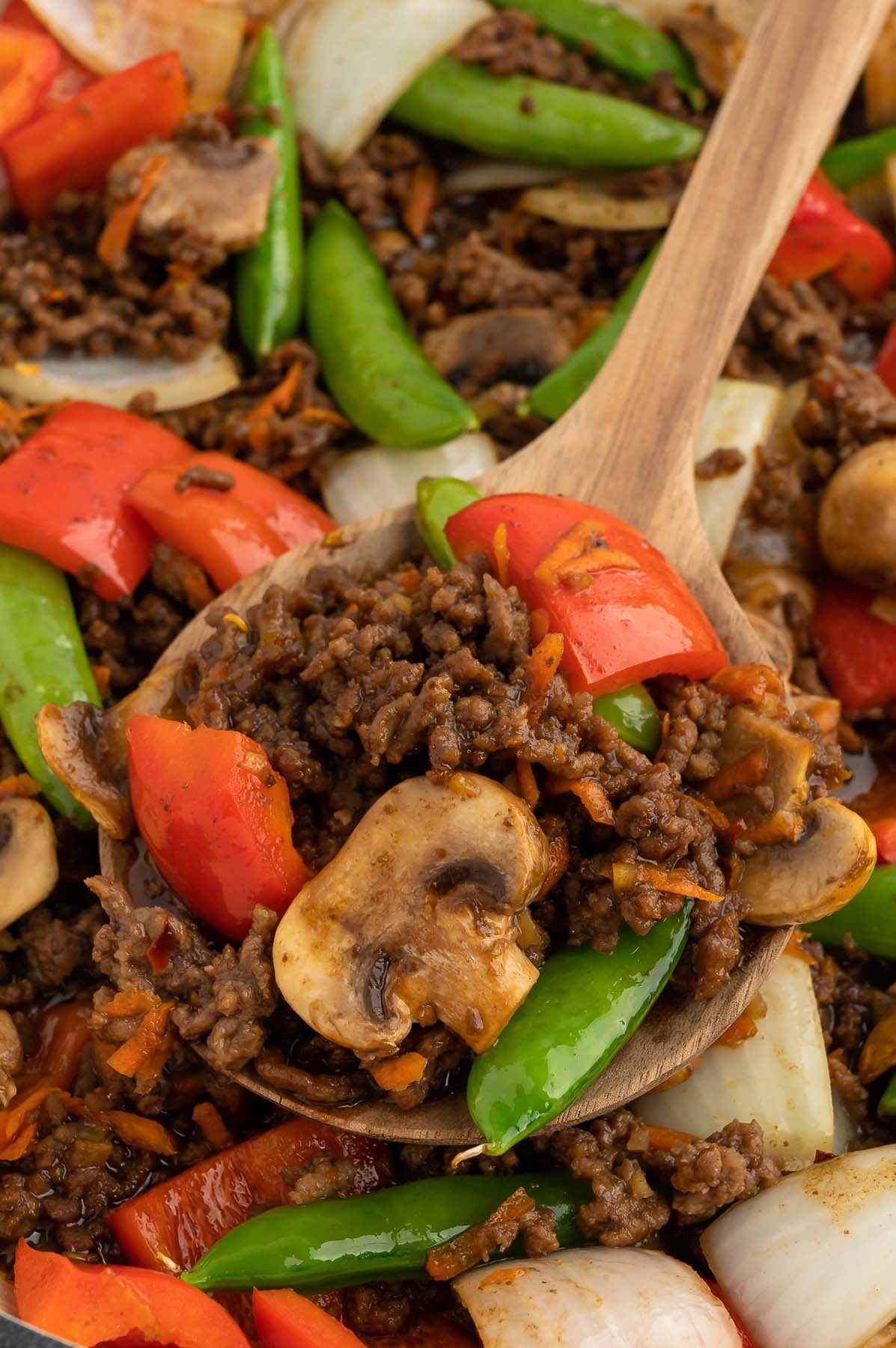A wooden spoon taking a scoop of ground beef stir fry from a skillet.