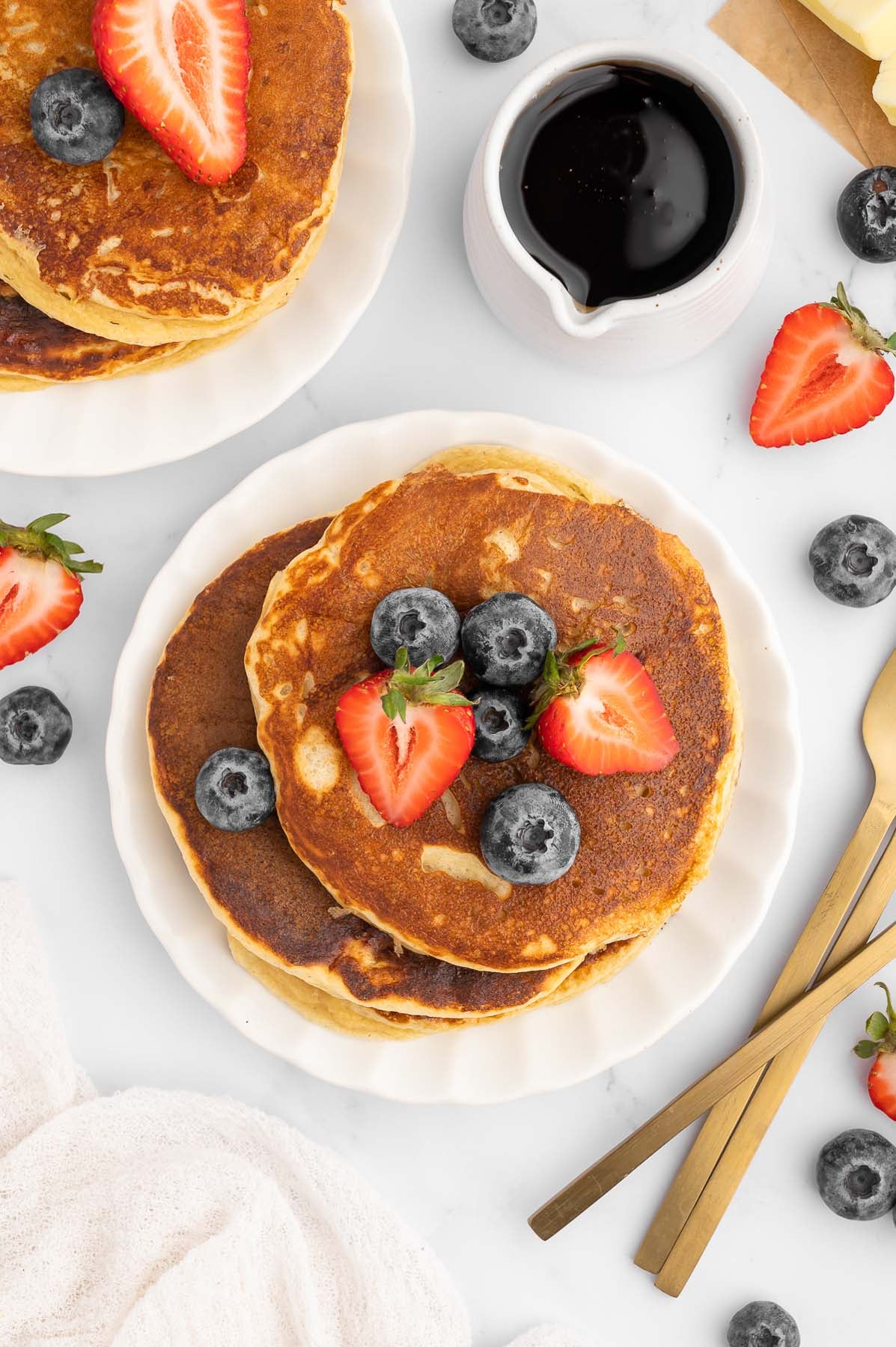 Overhead view of protein pancakes topped with fresh blueberries and strawberries, stacked on a white plate.