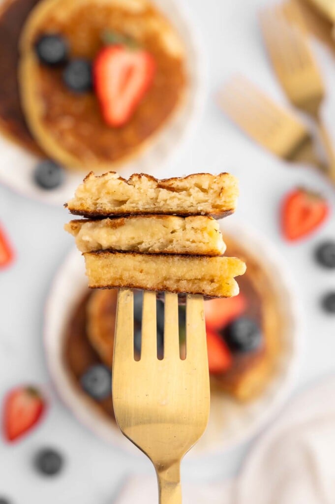 Three bites of fluffy protein pancakes being held up on a fork, close up to the camera.