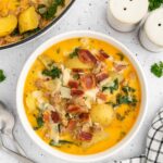 Healthy zuppa toscana in a white bowl with a dutch oven of the soup on the side on a white counter