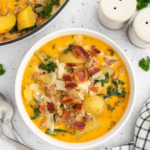 Healthy zuppa toscana in a white bowl with a dutch oven of the soup on the side on a white counter