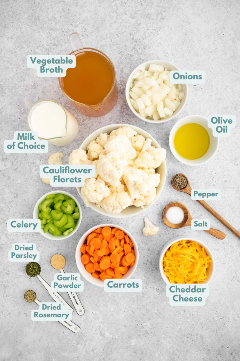 Ingredients for cauliflower soup recipe in white bowls: olive oil, onions, carrots, celery, cauliflower florets, vegetable broth, garlic powder, dried parsley, dried rosemary, salt, pepper, milk of choice, cheddar cheese