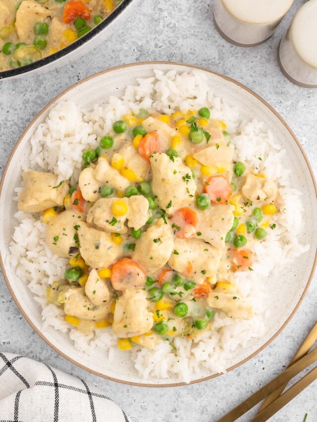 Crustless chicken pot pie on a bed of white rice on a plate on a white background with a dutch oven of the dish on the side.