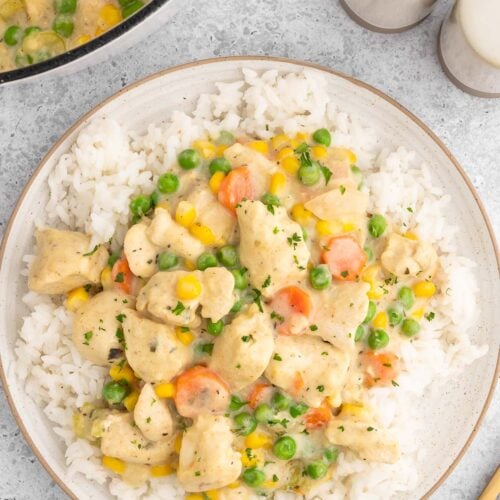 Crustless chicken pot pie on a bed of white rice on a plate on a white background with a dutch oven of the dish on the side.