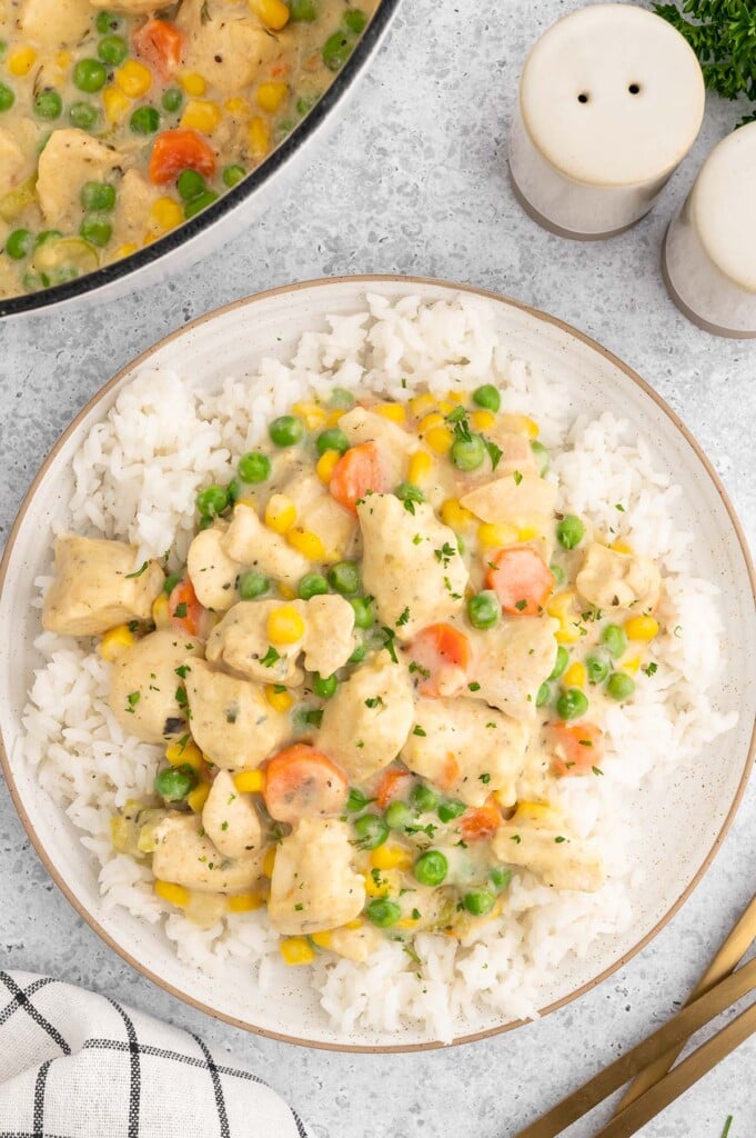 Crustless chicken pot pie on a bed of white rice on a plate on a white background with a dutch oven of the dish on the side.