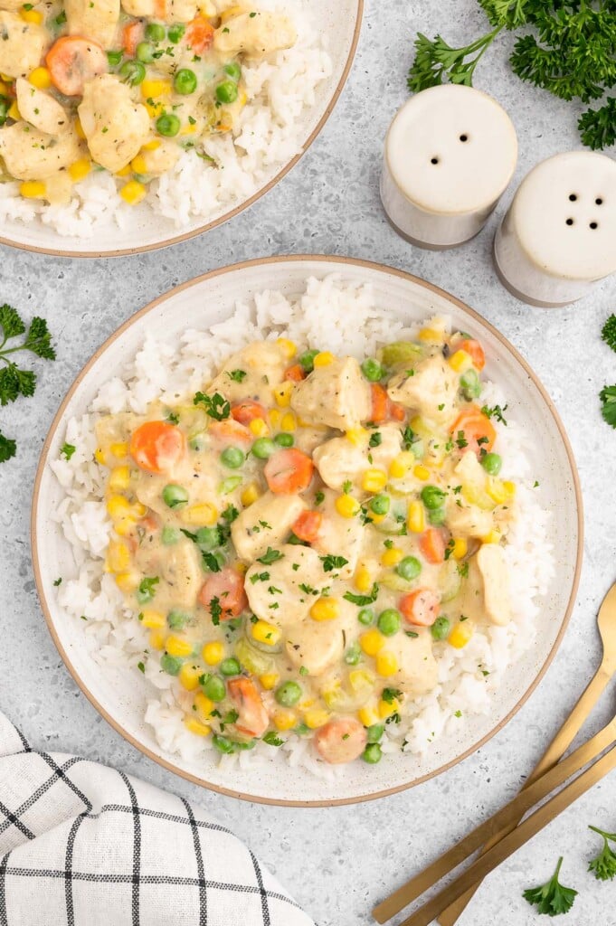 Crustless chicken pot pie on a bed of white rice on a plate on a white background with another plate on the side.